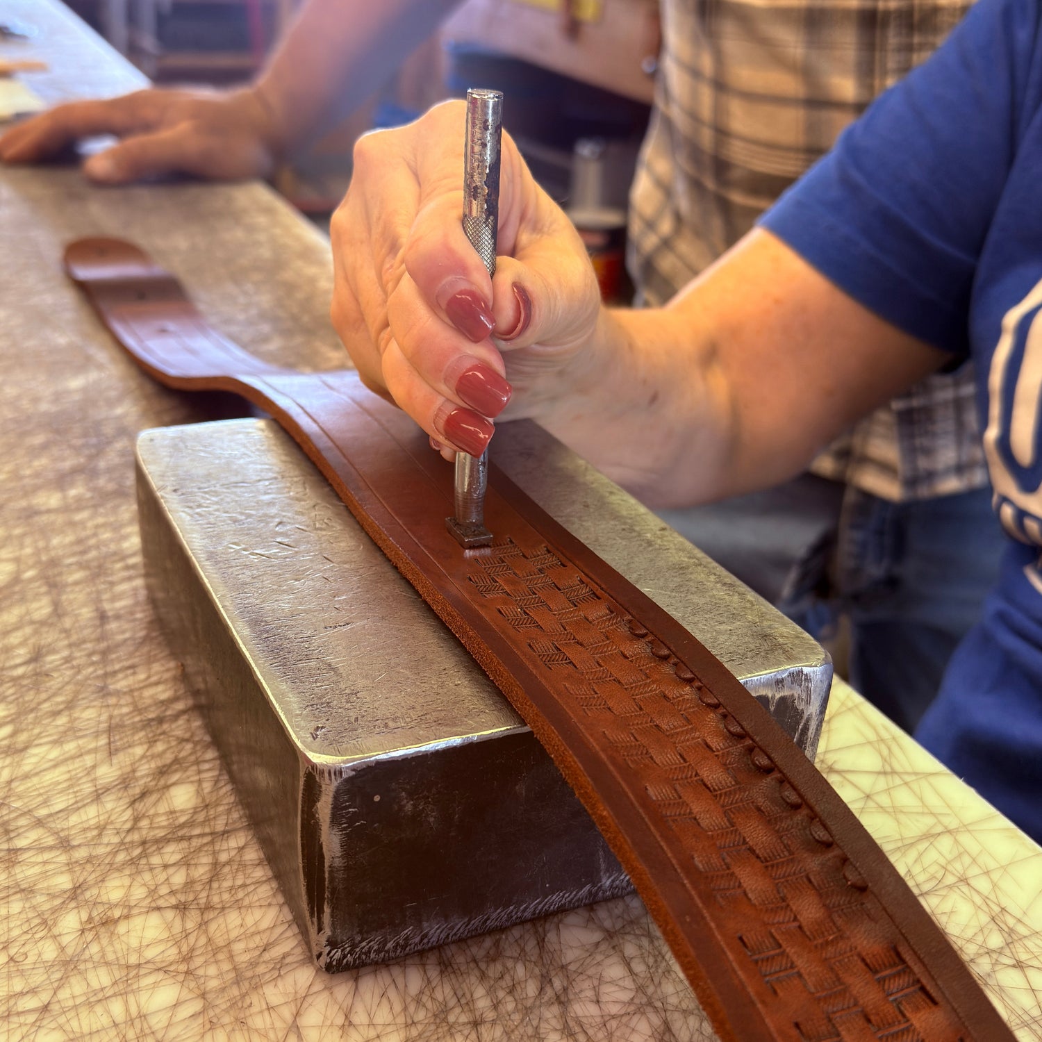 Person working on a leather product with a tool, likely in a workshop setting.