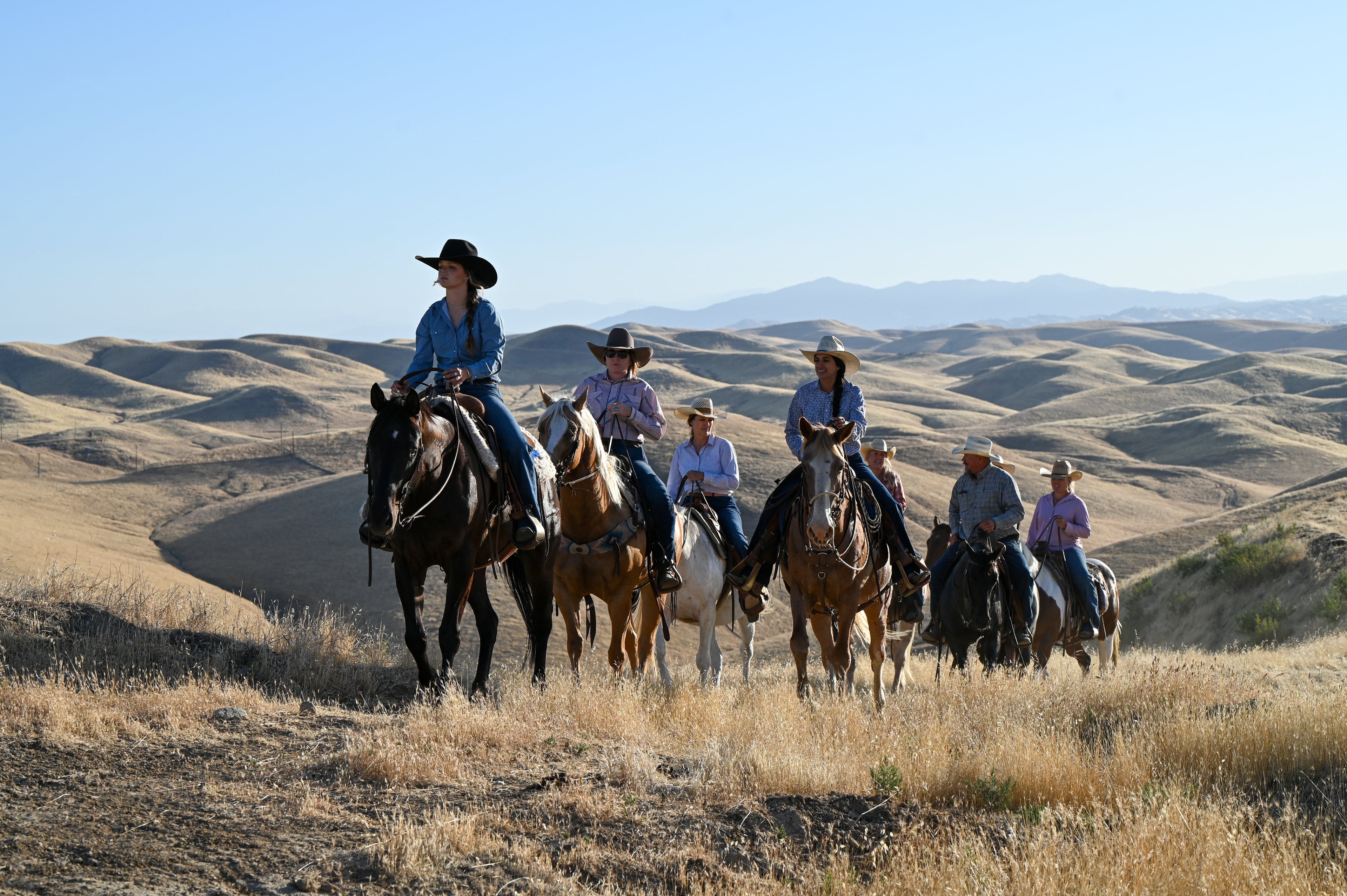 7 riders on horseback riding up a hill in the rolling foothills