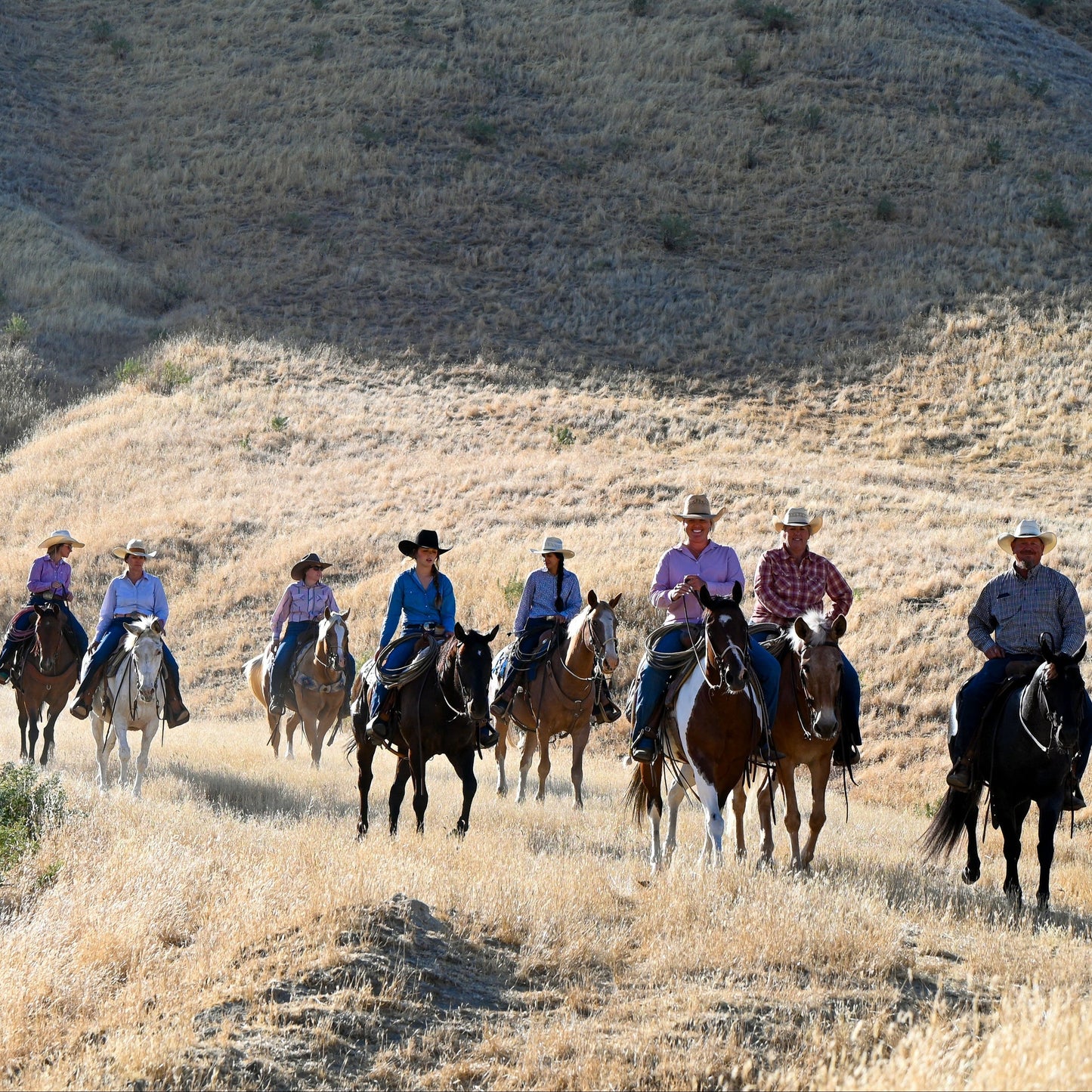 Group of people riding horses with mountains in the background