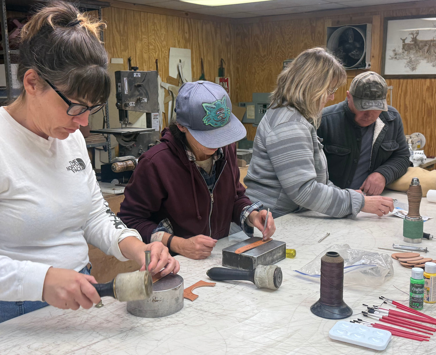 Four people working on a craft project at a table with tools and materials.