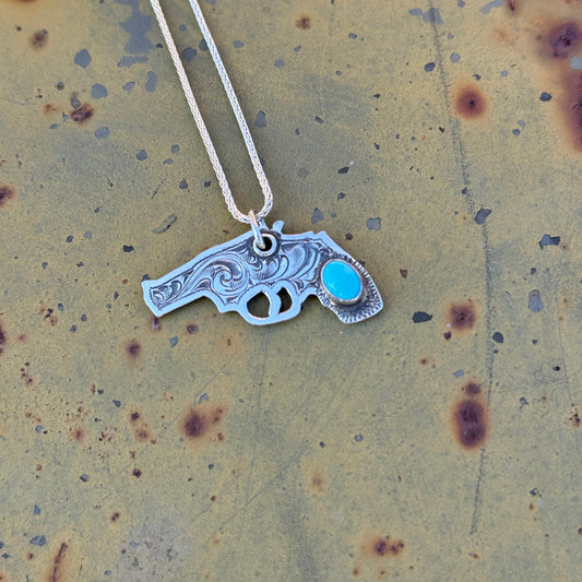 Silver revolver-shaped pendant with a blue gemstone on a textured beige surface