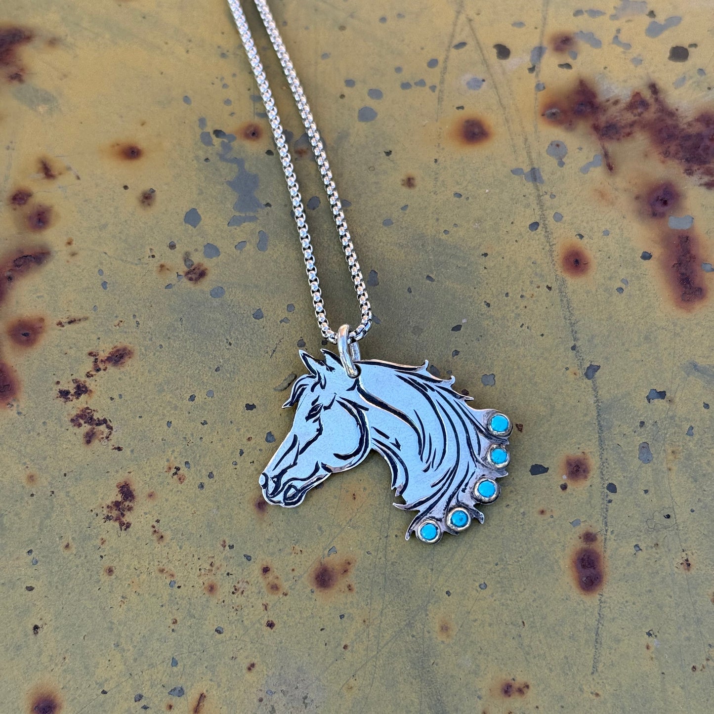 Silver Horse Head pendant with Turquoise Stones on metal backdrop