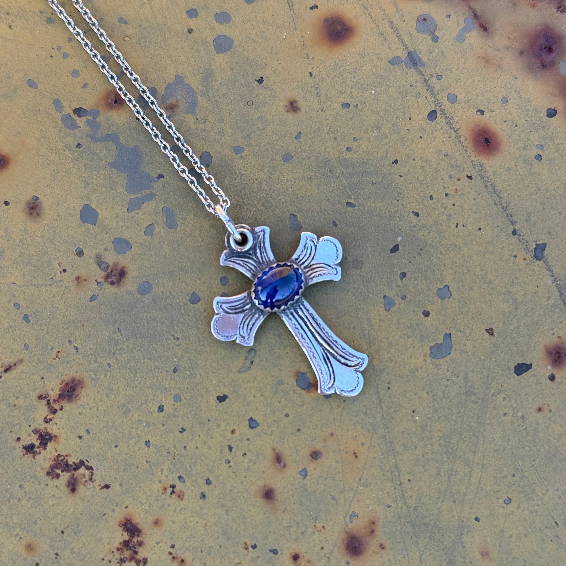 Silver cross pendant with a blue lapis gemstone on a textured surface 