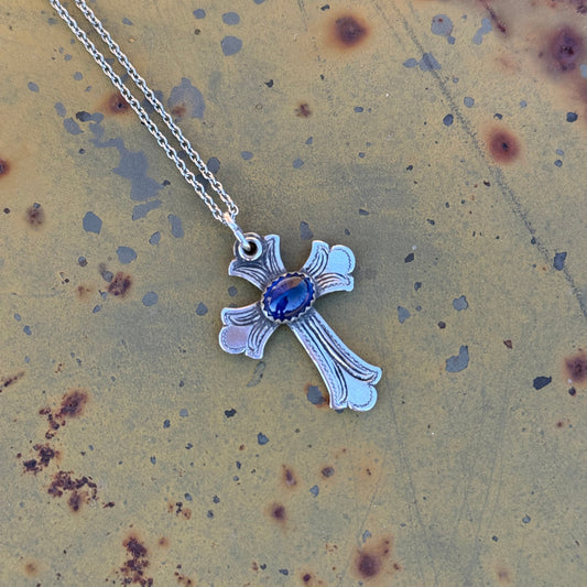 Silver cross pendant with a blue lapis gemstone on a textured surface 